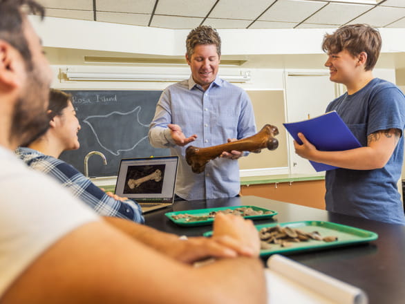 anthropology professor holding large bone in front of students