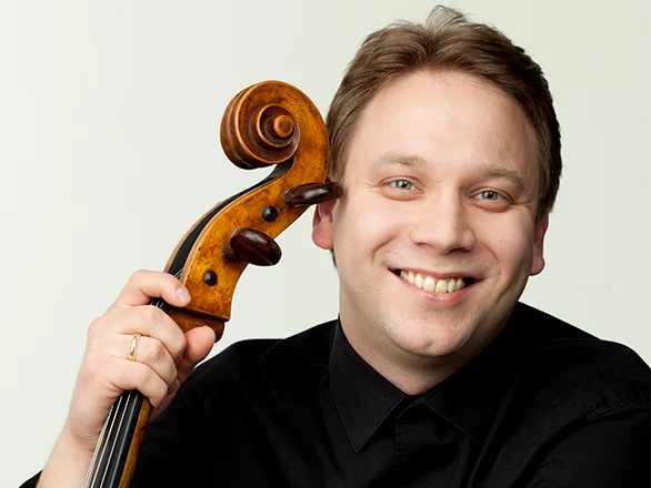Dmitri Atapine holds the top of a cello while wearing a black shirt to pose for a promotional photo.