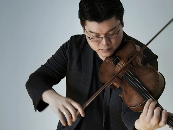 Che-Yen Chen wears a black suit and glasses while playing a violin.