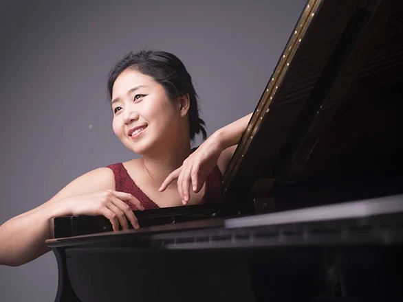Hyeyeon Park rests her arms on a piano while posing for a photo.