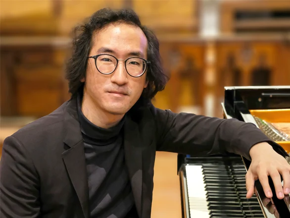 Sahun Sam Hong rests his arm on a piano while seated.