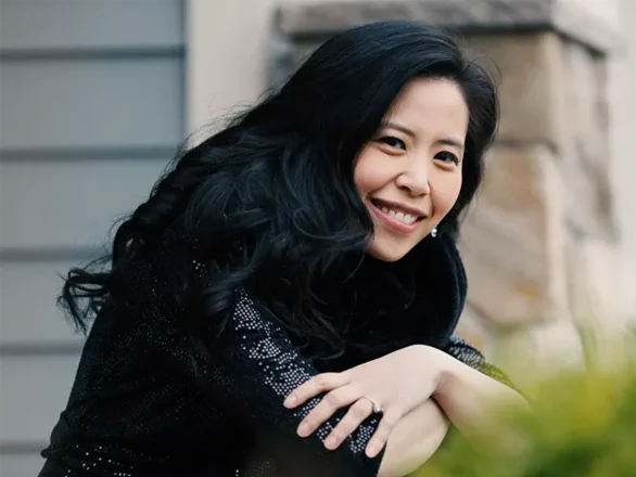 Gloria Chien wears a black shirt and poses for a photo with her arms crossed on a railing.