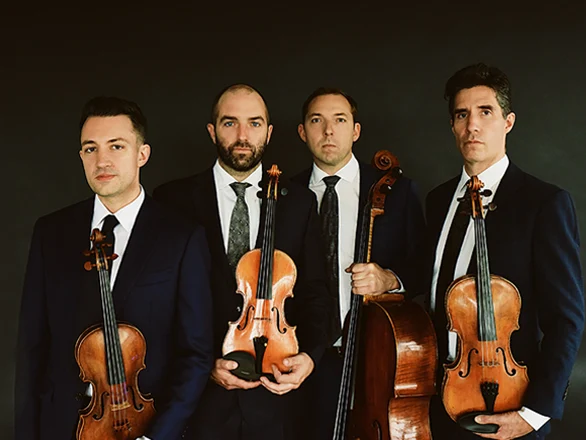 The four members of the Escher Quartet hold violins while wearing suits and stand for a publicity photo.