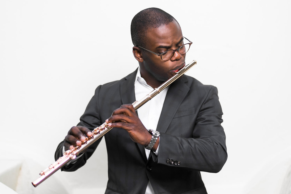 Demarre McGill wears a gray suit and glasses while playing the flute.