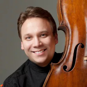 Dmitri Atapine poses for a headshot while holding a cello