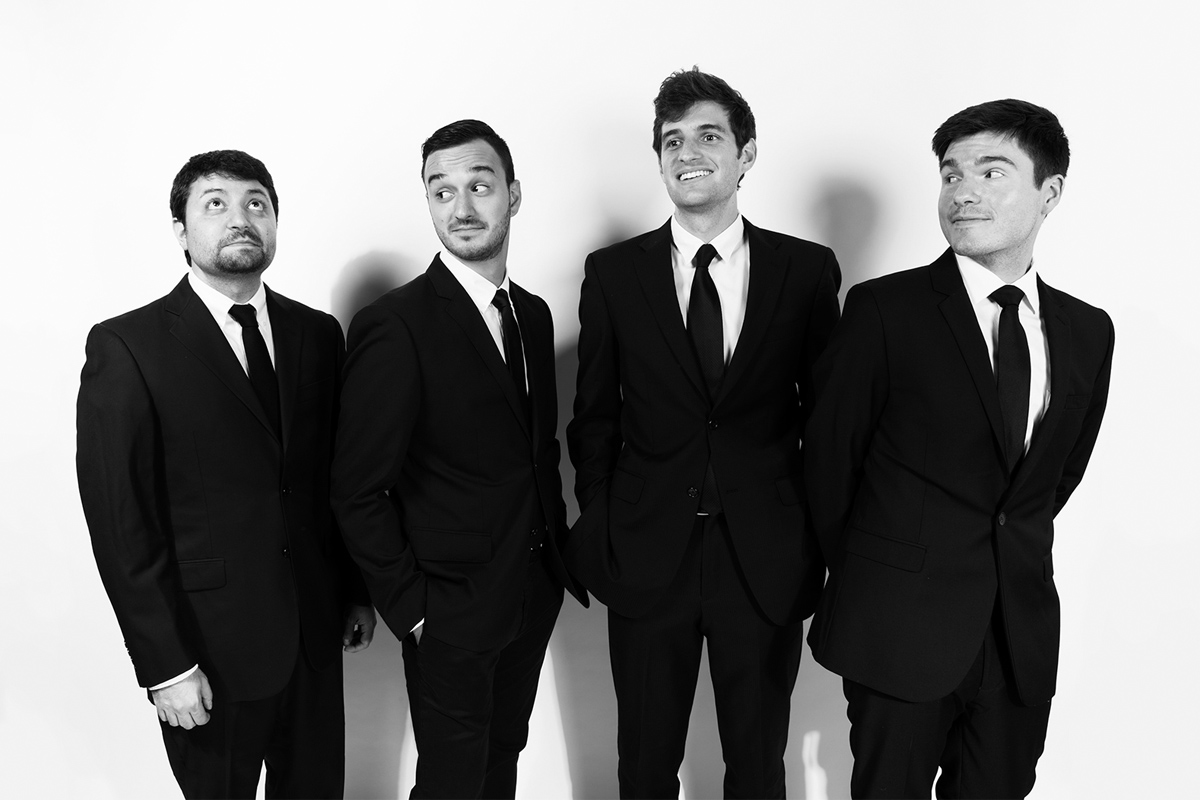 The members of Sandbox Percussion pose for a black and white photo while wearing suits and ties.