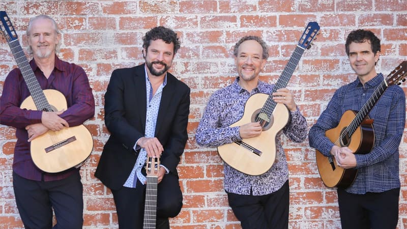 The four members of the Los Angeles Guitar Quartet pose with their guitars in front of a brick wall.