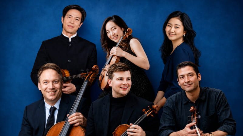 six musicians holding instruments with blue background