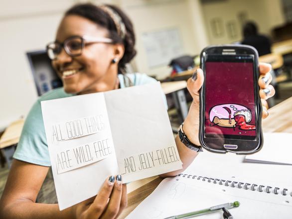 girl holding white folded paper with phone next to it
