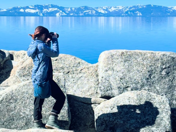 woman standing on rocks looking at lake tahoe with binoculars