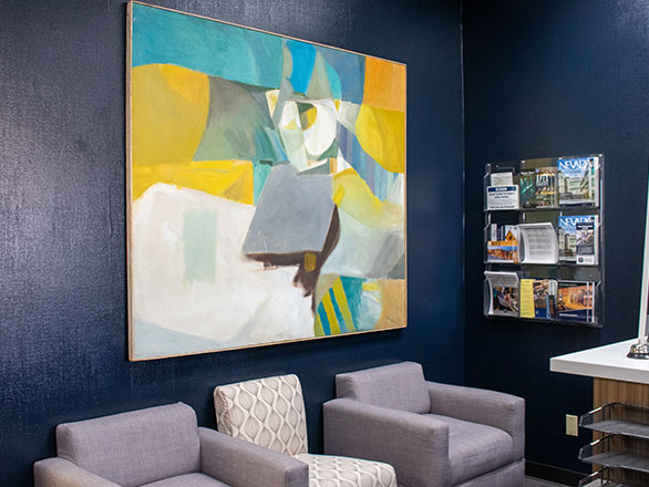 A large colorful abstract painting hangs on an office wall with chairs in front of it