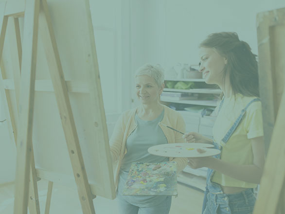 Elderly person learning to paint with younger individual