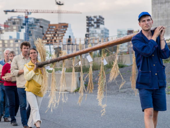 people carrying pole with straw hanging off with cityscape in background