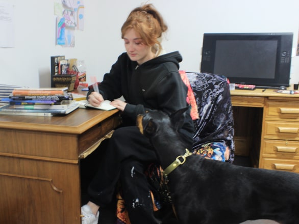 woman sitting at a desk writing with a dog to her left