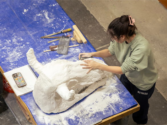 Two students in the sculpture studio wear protective welding gear