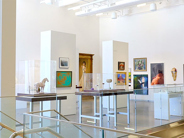 Art museum room filled with art hanging on the walls and glass display cases with sculptures and figurines