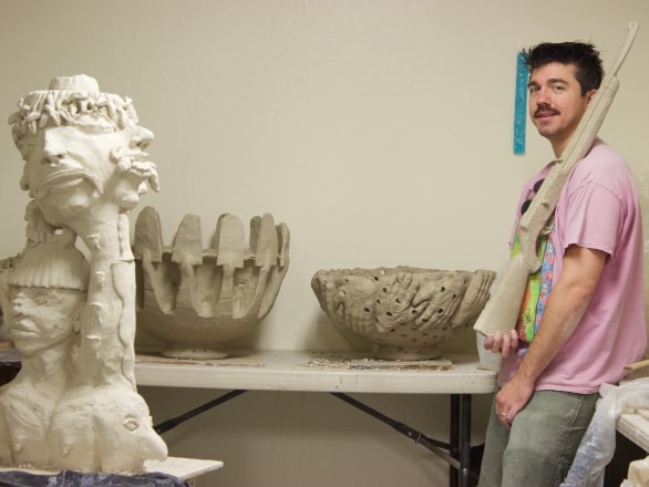 trent standing holding model gun in art room with sculptures