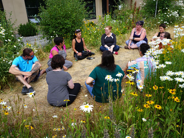 Group of students and faculty sitting in grass and wildflowers talking.