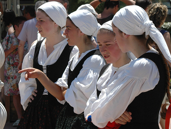 Four Basque women dressed in Basque clothing talk to one another