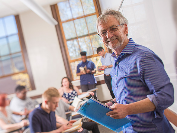 Professor David Fenimore holds clipboard and teaches class