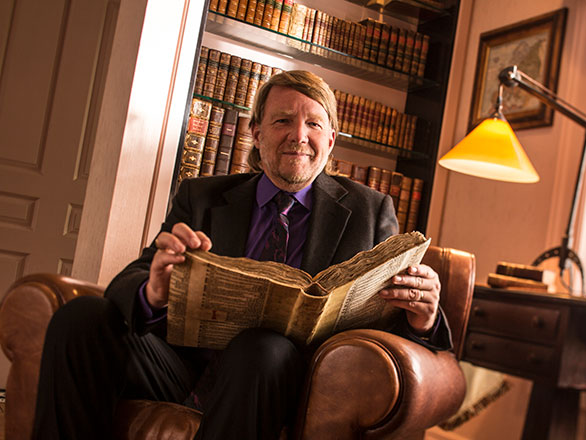 Professor Rasmussen sits in office holding old literature book