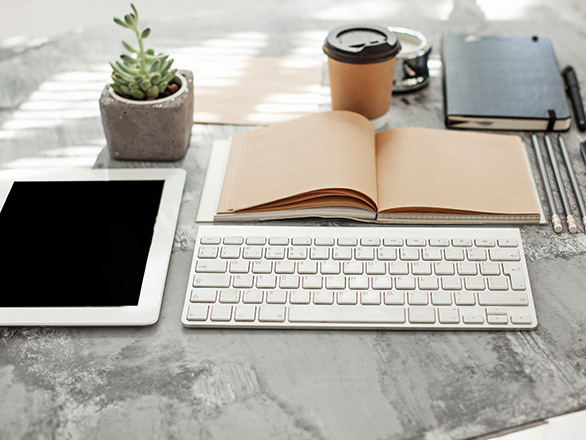 Tablet, keyboard, plant, open blank book, coffee closed notebook and pencils sit on a marble desk