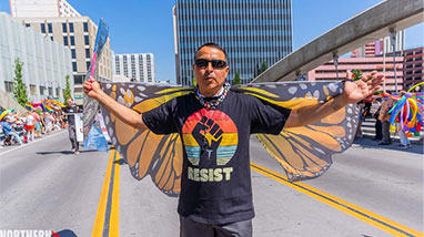 Daniel Enrique Perez stands in street holding up butterfly wings during Pride march