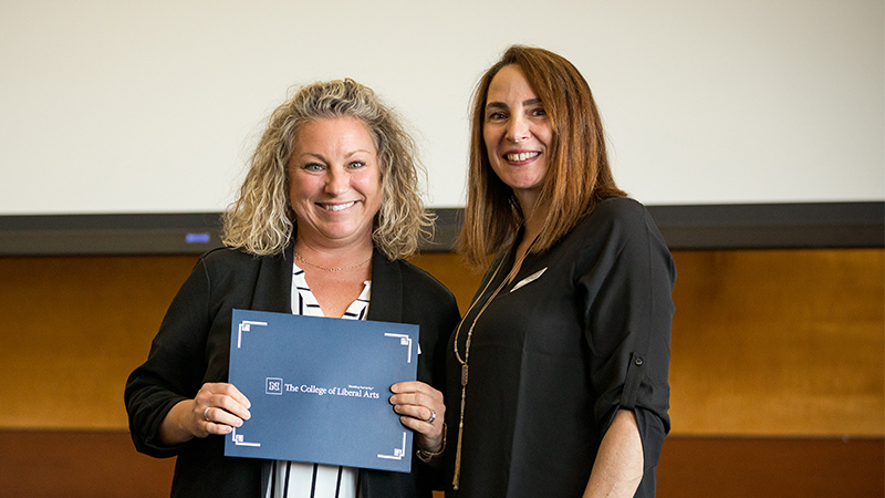 two women smiling at camera, one holding an award