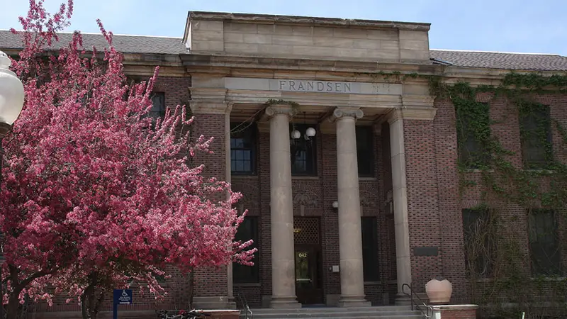 Exterior of Fransden Hall, a brick building with four white columns at the entrance surrounded by trees and bushes.