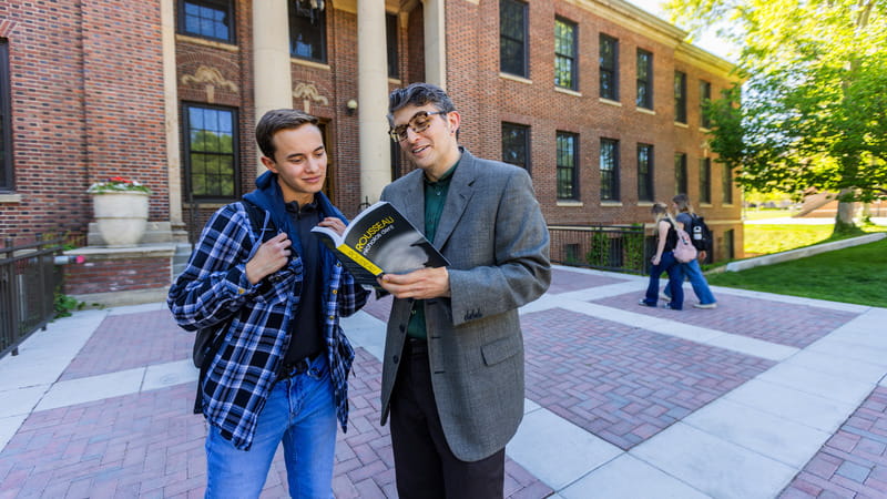 student and professor reading philosophy book outside