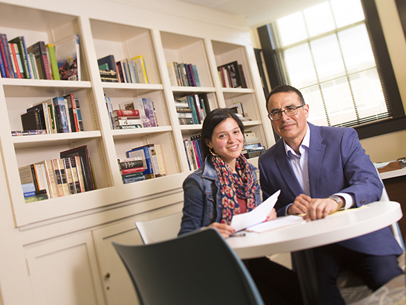 Jeannette and Daniel looking over paper with bookshelf behind them