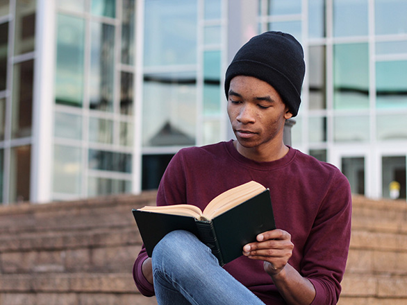 Man sitting outside on bench reading book