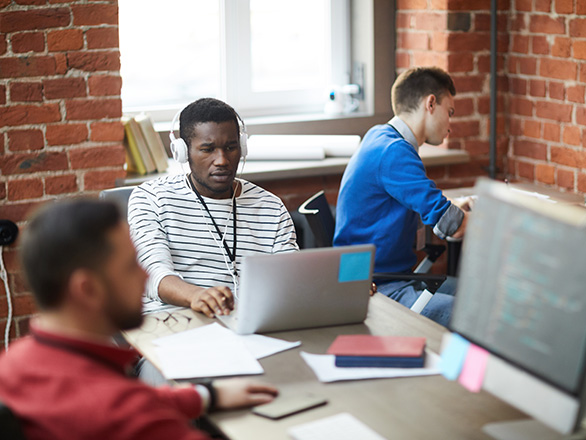 Three people sitting around computers working together