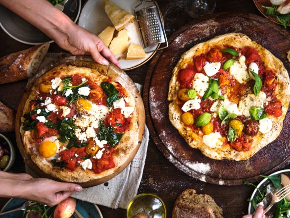 person setting pizza on table with another pizza next to it