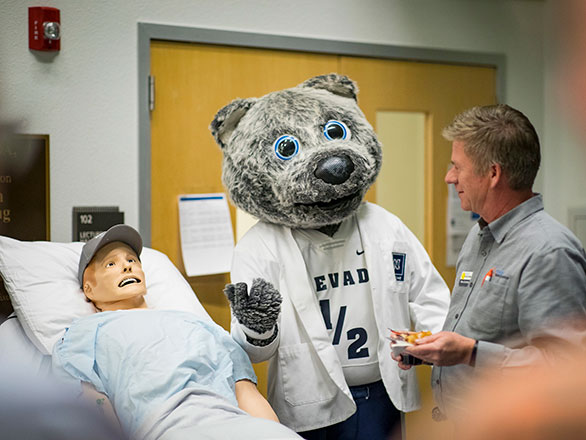 A doctor and mascot Wolfie look over robotic patient in hospital room