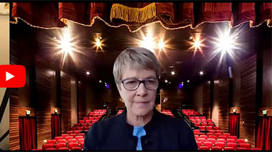 Debra Moddelmog on Zoom screen with empty theatre behind her