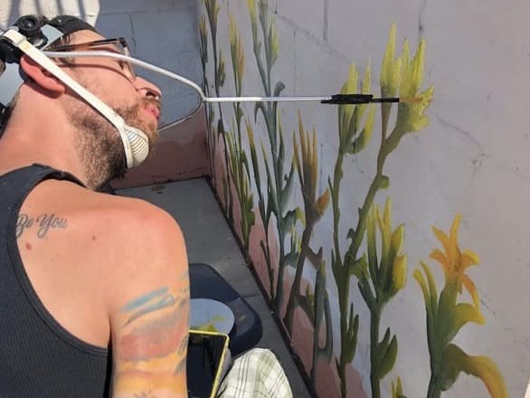 man painting wall with a mouth device