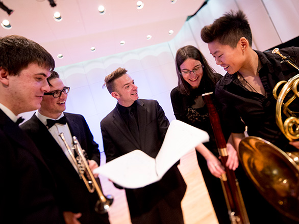 Music professor conducting looking over score with student band members on stage