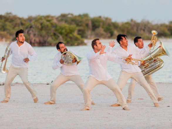Five brass musicians play instruments outside by pool