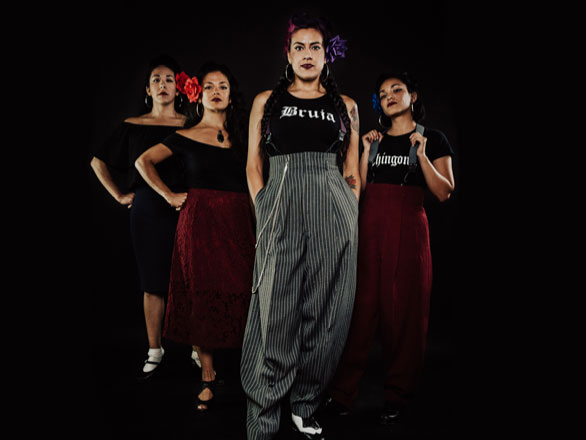 Pachuquísmo group standing on stage during performance in zoot suits