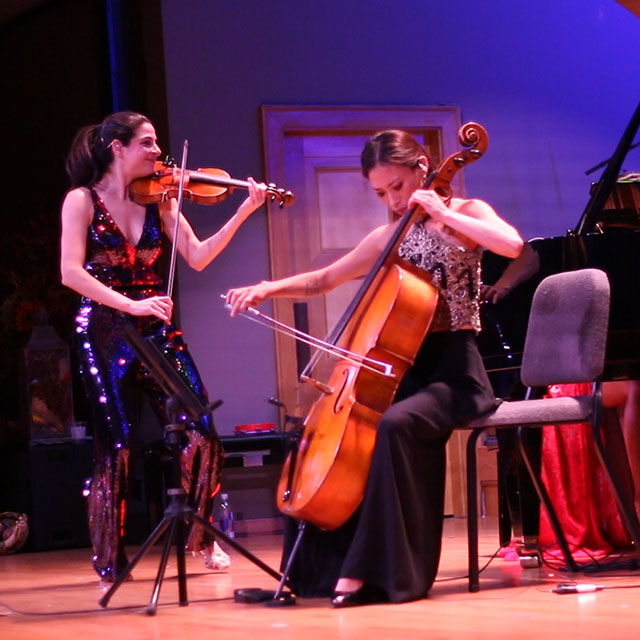 Two women play a violin and a cello on stage during a performance