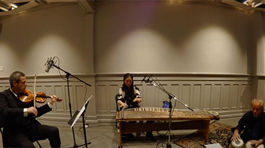 Yumi playing instrument in room with violinist and percussionist