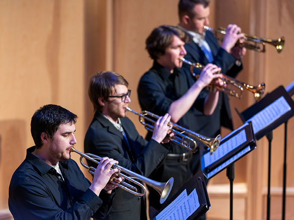 Four trumpet players in a line, trumpets raised
