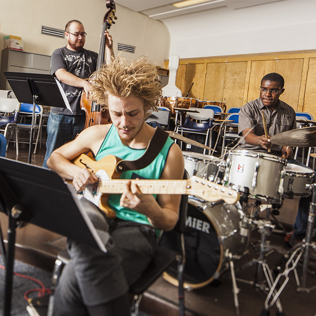 Three men play guitar, bass and drums inside a rehearsal room