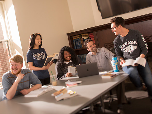 Students sit around table with professor inside the classroom having a discussion
