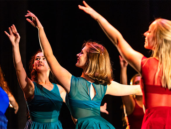 Five dancers in colorful dresses perform on stage.