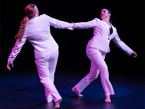 Two dancers in white suits perform on stage