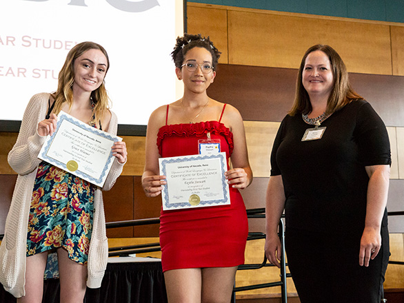 Two female students stand on stage with Arabic awards from professor