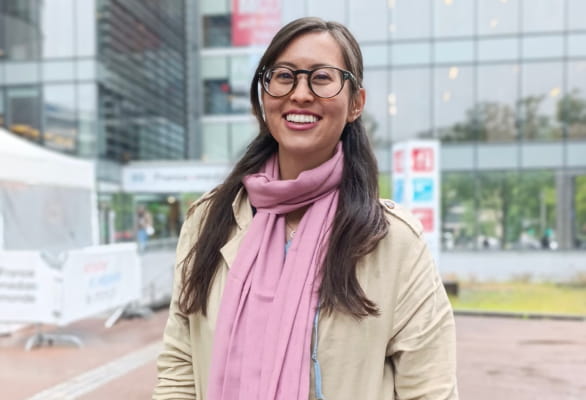 woman with glasses and pink scarf smiling in front of glass building