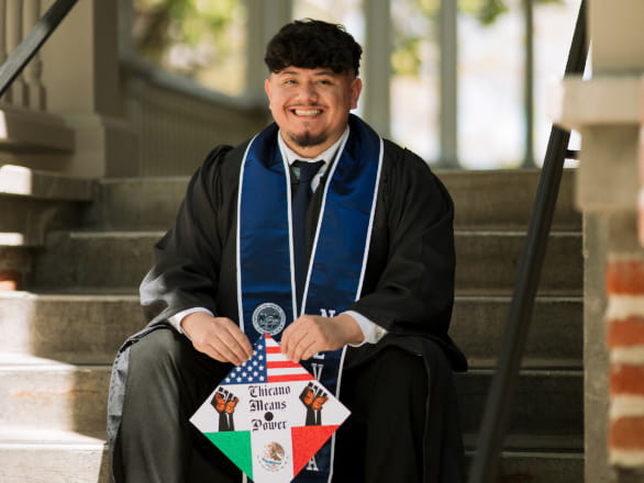 oscar lopez armenta sitting on stairs in graduation stole holding cap